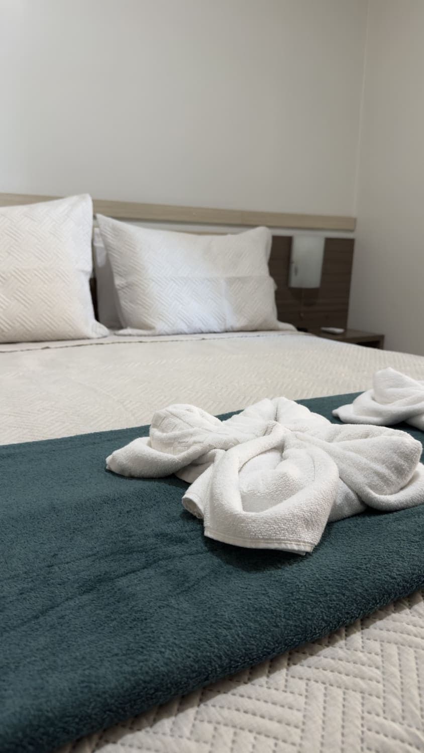 Cama Queen com enxoval branco e detalhe em verde no Apartamento Luxo Casal